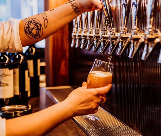 Tattooed arm pouring a glass of tap beer at our Des Moines restaurant