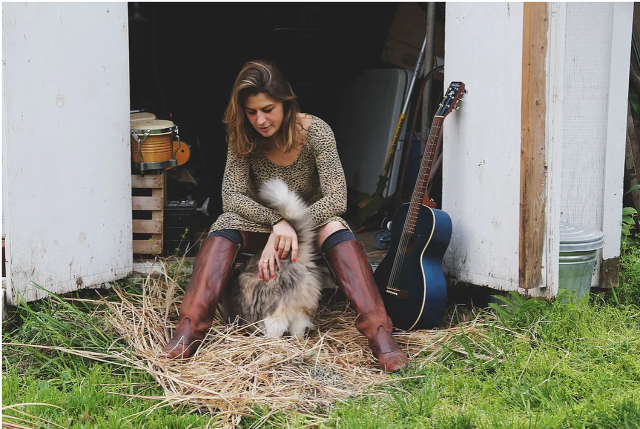 Female musician Jordan Sellergren petting a fluffy cat with her black guitar next to her in Des Moines