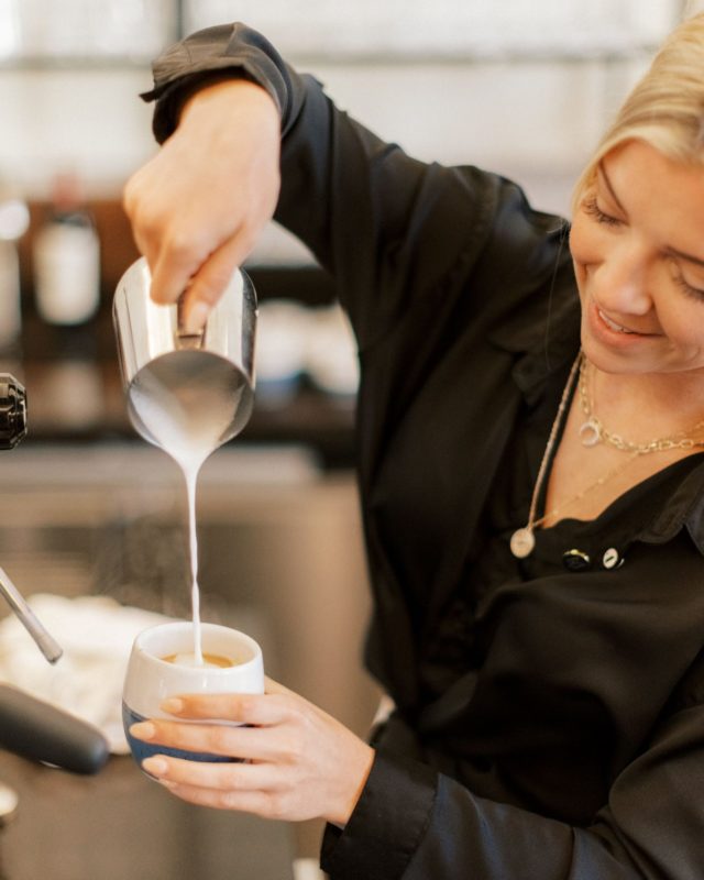 Female Barista pouring foam milk into a coffee cup at our coffee shop in des Moines, IA