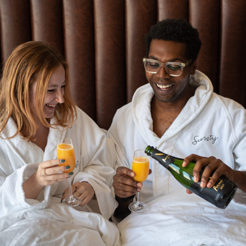 Couple drinking mimosas in bed at our boutique hotel in Des Moines
